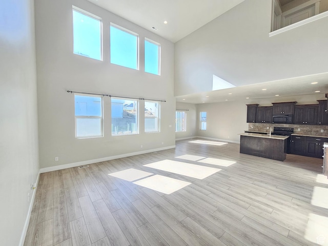 unfurnished living room with baseboards, a healthy amount of sunlight, light wood finished floors, and high vaulted ceiling