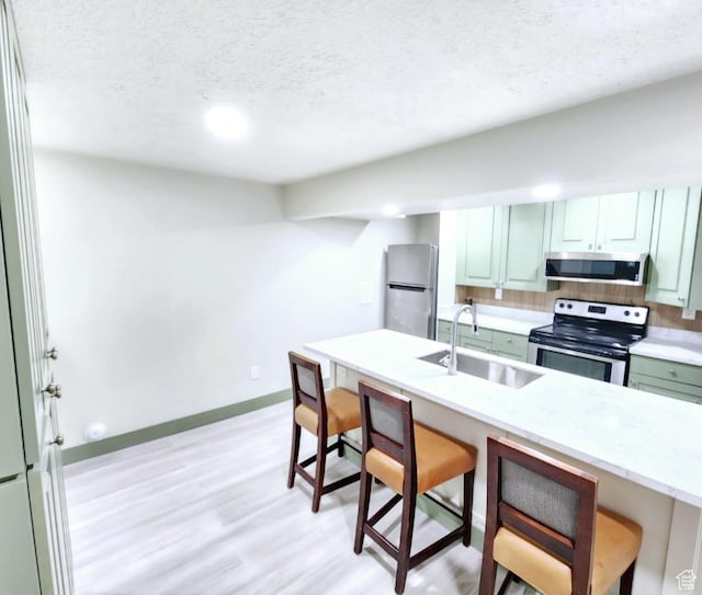 kitchen with a breakfast bar, a sink, light wood-style flooring, a textured ceiling, and appliances with stainless steel finishes