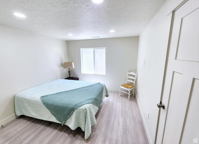 bedroom featuring light wood finished floors, baseboards, recessed lighting, and a textured ceiling