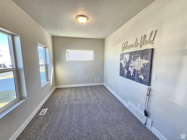 carpeted spare room with baseboards, a textured ceiling, and visible vents