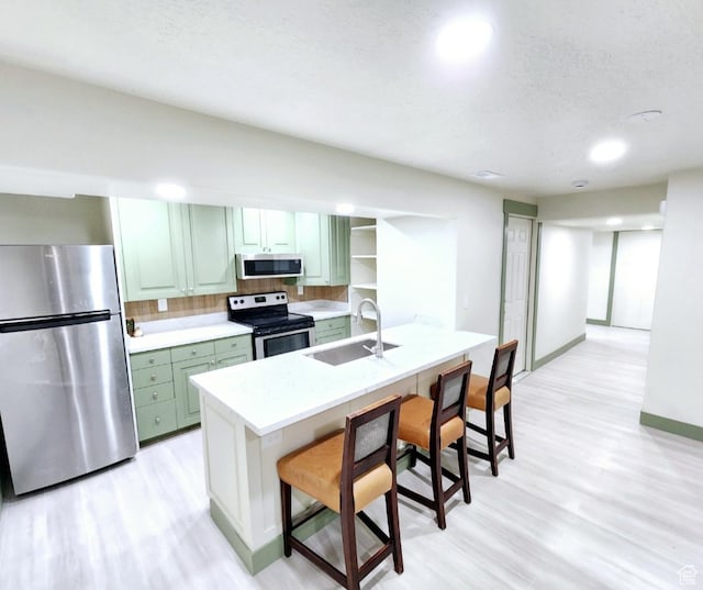 kitchen with light wood-style flooring, a sink, green cabinetry, light countertops, and appliances with stainless steel finishes
