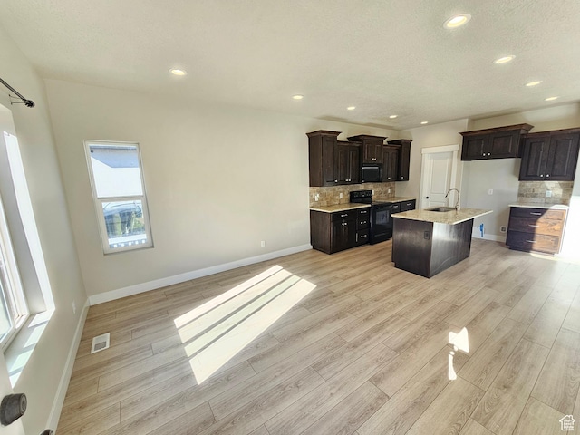 kitchen with visible vents, a sink, light wood-type flooring, black appliances, and tasteful backsplash