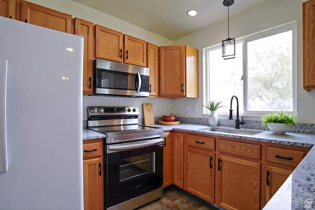 kitchen with stainless steel appliances, a sink, hanging light fixtures, and light stone counters