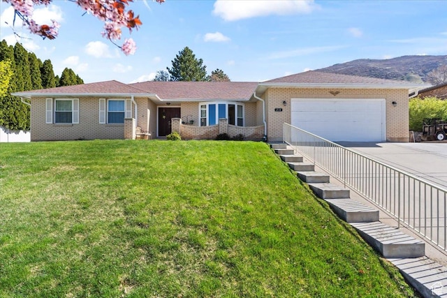 ranch-style house featuring concrete driveway, an attached garage, brick siding, a front yard, and a mountain view