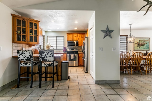 kitchen featuring tasteful backsplash, glass insert cabinets, a kitchen bar, a peninsula, and appliances with stainless steel finishes