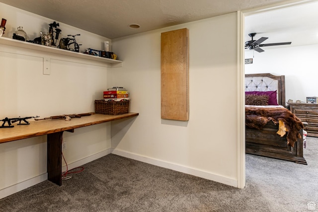 interior space with dark colored carpet, baseboards, built in desk, and a ceiling fan