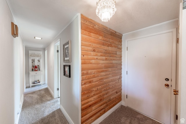 corridor featuring wooden walls, an inviting chandelier, carpet, baseboards, and ornamental molding