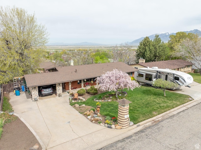single story home featuring a chimney, a shingled roof, concrete driveway, a front yard, and a mountain view