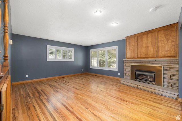 unfurnished living room featuring baseboards, a stone fireplace, and wood finished floors