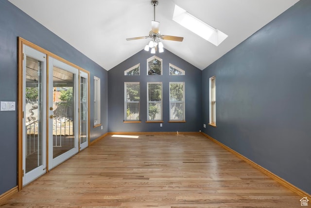 empty room with ceiling fan, a wealth of natural light, vaulted ceiling with skylight, and light wood-style flooring