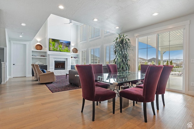 dining space with light wood-style flooring, a textured ceiling, recessed lighting, built in shelves, and a brick fireplace