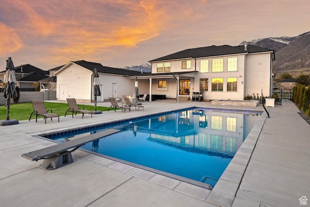 back of property at dusk with fence, an outdoor pool, a patio area, and a mountain view