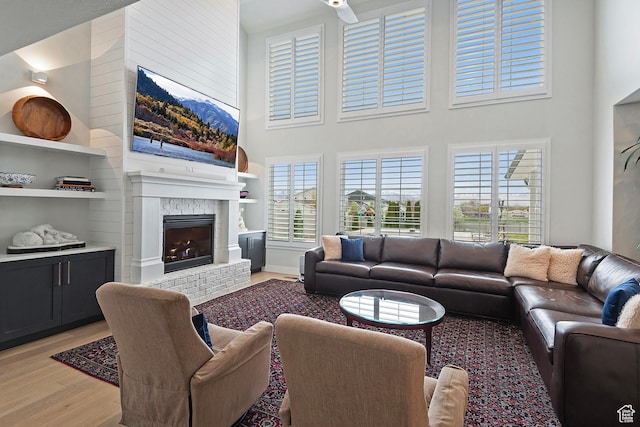 living area with a brick fireplace, a towering ceiling, light wood finished floors, and built in features