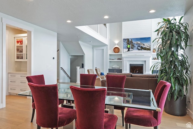 dining space with a fireplace, recessed lighting, built in features, and light wood-style flooring