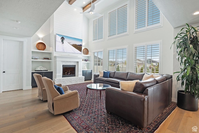 living room with light wood-style flooring, a towering ceiling, built in features, baseboards, and a fireplace