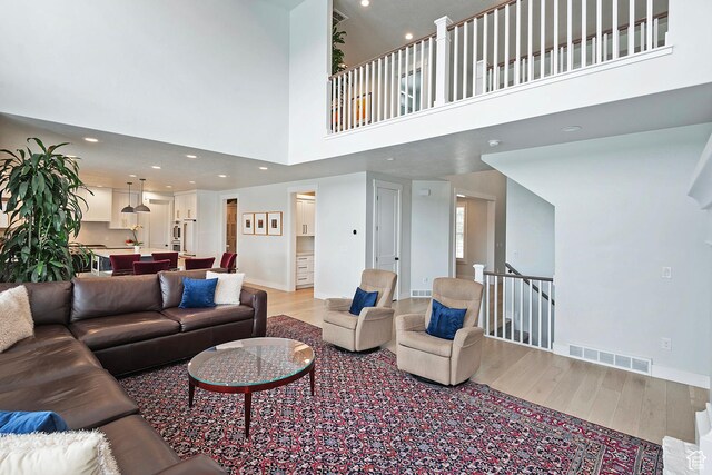 living room with a high ceiling, light wood-style flooring, visible vents, and recessed lighting