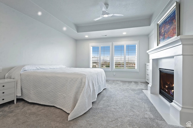 bedroom with a fireplace with flush hearth, recessed lighting, carpet, a tray ceiling, and ceiling fan