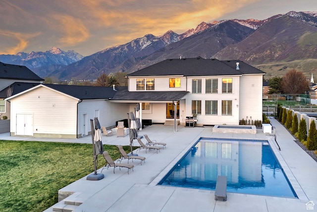 back of house at dusk with a fenced backyard, a yard, a mountain view, and a patio