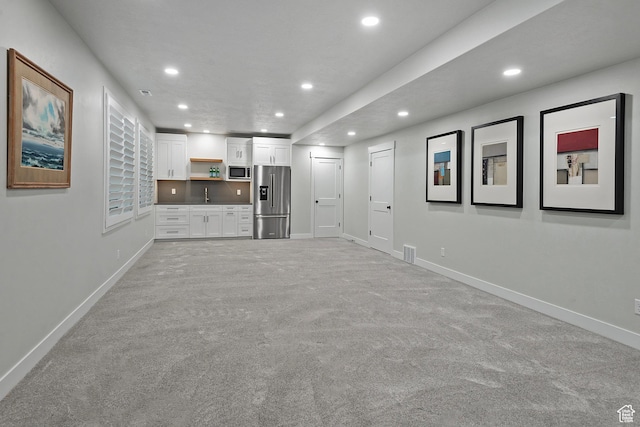 unfurnished living room with light carpet, a sink, visible vents, baseboards, and recessed lighting