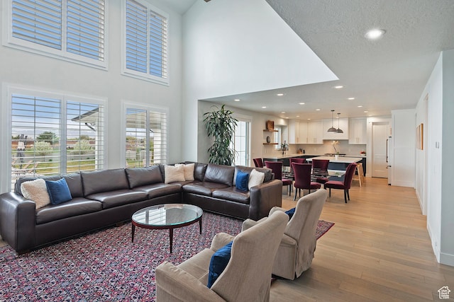 living area with light wood finished floors, a towering ceiling, baseboards, and recessed lighting