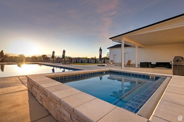 pool at dusk with an outdoor pool and a patio