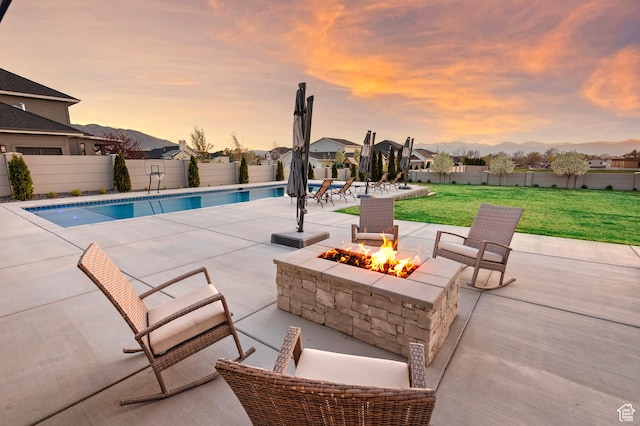 pool at dusk featuring a lawn, an outdoor fire pit, a fenced backyard, a fenced in pool, and a patio