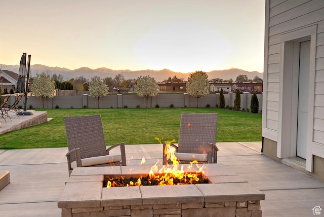 patio terrace at dusk with a fire pit, a yard, a fenced backyard, and a mountain view