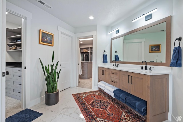 bathroom with a spacious closet, visible vents, baseboards, and a sink