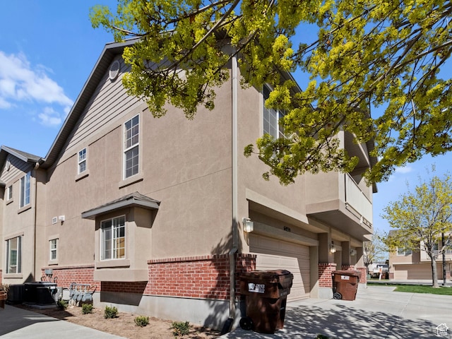6939 S Tourist Ln W Unit 2C, West Jordan, UT 84084 - view of side of home with central air condition unit, concrete driveway, brick siding, an attached garage, and stucco siding