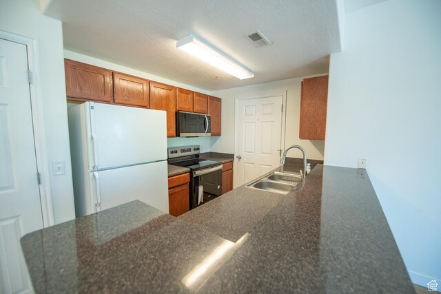 kitchen featuring a peninsula, a sink, visible vents, brown cabinetry, and appliances with stainless steel finishes