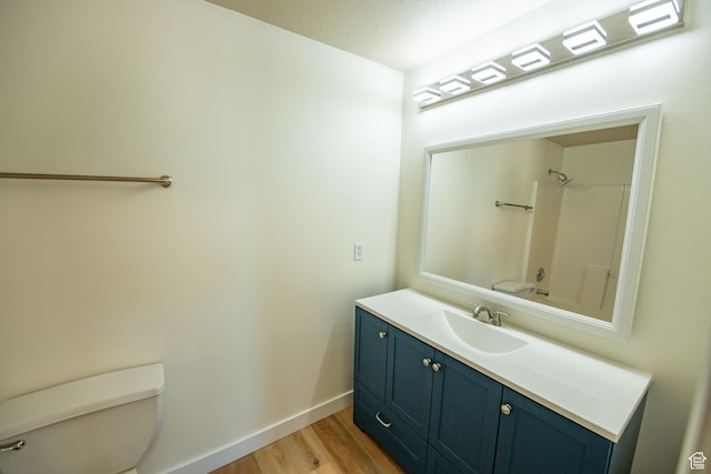 bathroom with toilet, vanity, wood finished floors, and baseboards