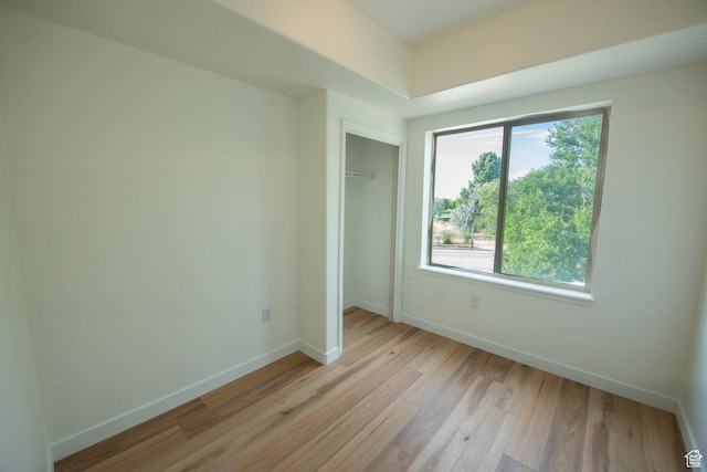 unfurnished bedroom featuring light wood-style flooring, baseboards, and a closet
