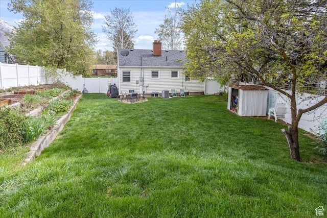 rear view of property with a fenced backyard, a garden, a yard, an outdoor structure, and a storage unit