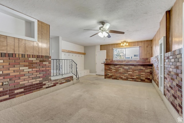 unfurnished living room featuring brick wall, a ceiling fan, wood walls, and light carpet