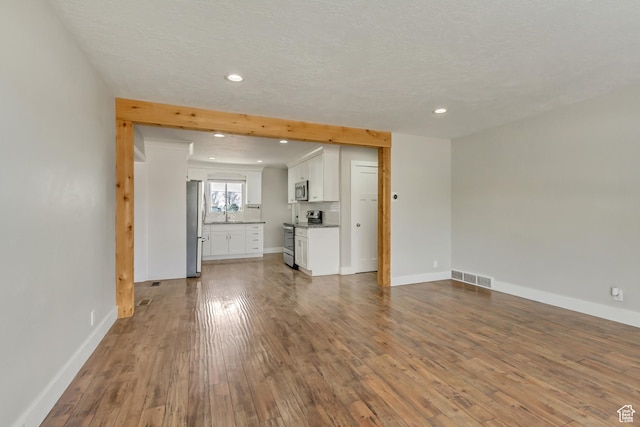 unfurnished living room with a sink, wood finished floors, baseboards, visible vents, and recessed lighting