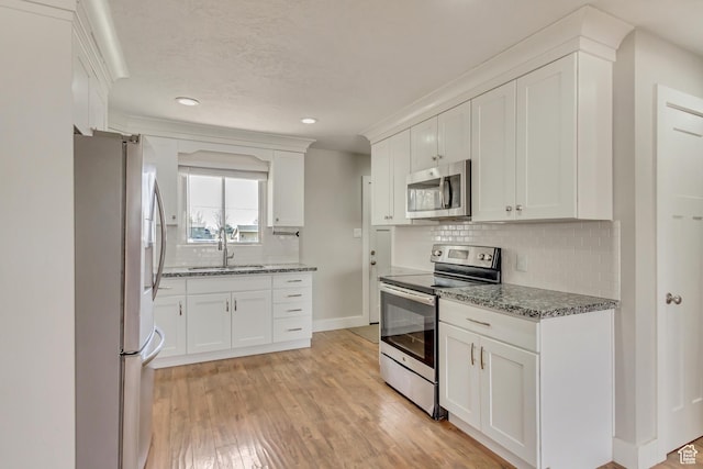 kitchen featuring stainless steel appliances, a sink, light wood-type flooring, stone counters, and white cabinetry