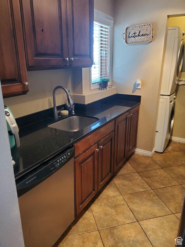 kitchen with stainless steel dishwasher, a sink, dark countertops, stacked washer / drying machine, and light tile patterned floors