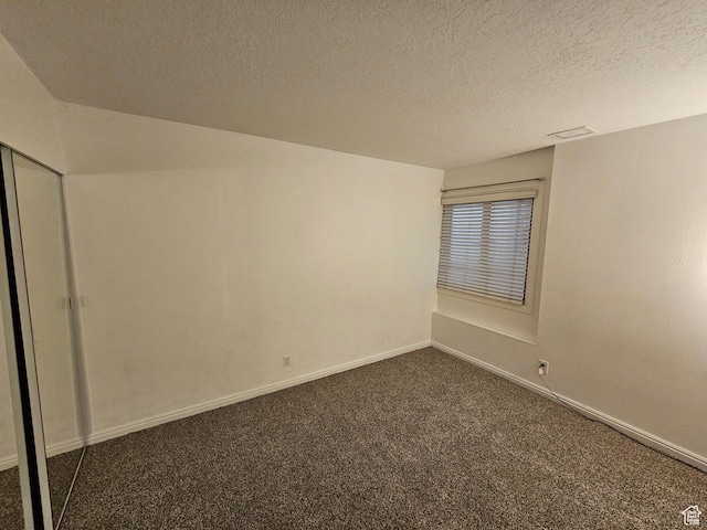 spare room with dark carpet, baseboards, visible vents, and a textured ceiling