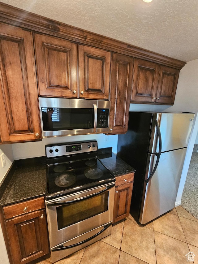 kitchen with light tile patterned flooring, a textured ceiling, dark stone counters, and stainless steel appliances