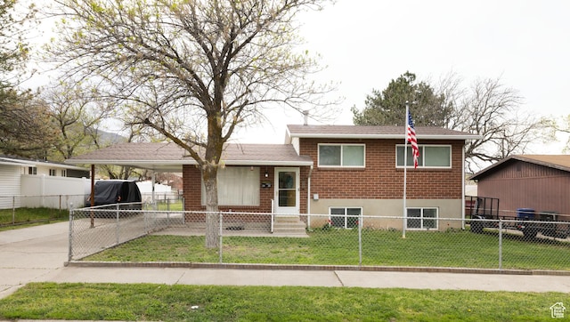 split level home featuring a fenced front yard, driveway, a carport, brick siding, and a front yard