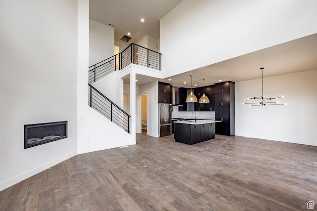 unfurnished living room featuring stairway, wood finished floors, a towering ceiling, baseboards, and a notable chandelier