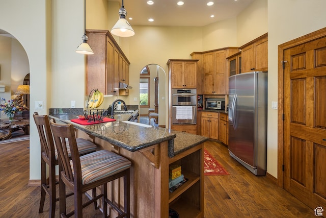 3270 E Rim Vistas Cir, Moab, UT 84532 - kitchen featuring brown cabinetry, a high ceiling, arched walkways, a peninsula, and appliances with stainless steel finishes