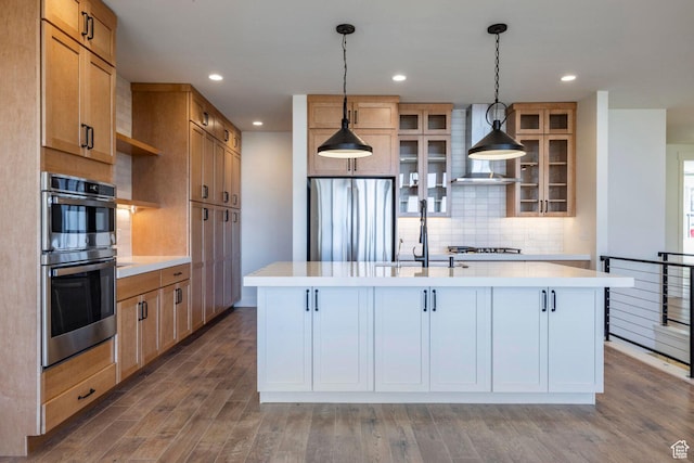 kitchen featuring light countertops, wall chimney range hood, a sink, decorative backsplash, and appliances with stainless steel finishes