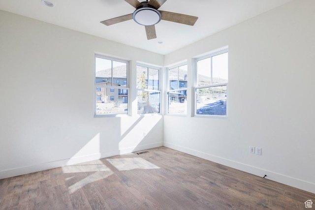 empty room with wood finished floors, baseboards, a ceiling fan, and a healthy amount of sunlight