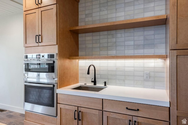 kitchen featuring a sink, tasteful backsplash, open shelves, light countertops, and double oven