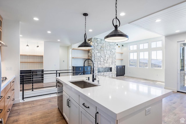 kitchen featuring stainless steel dishwasher, a sink, light wood-type flooring, open floor plan, and a stone fireplace