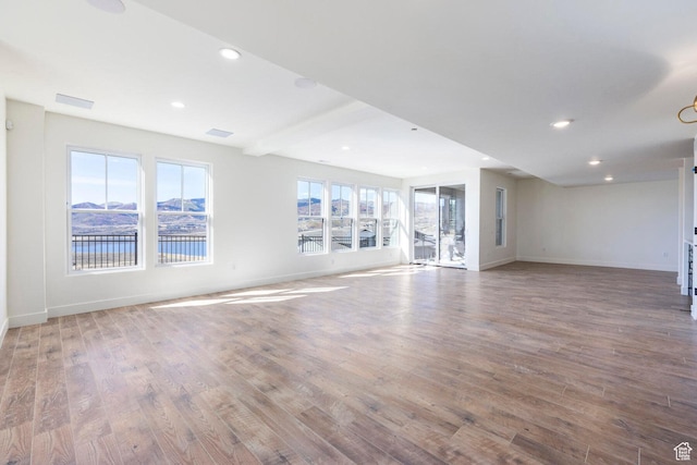 unfurnished living room with beam ceiling, wood finished floors, baseboards, and recessed lighting