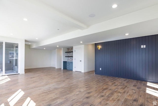 unfurnished living room with recessed lighting, wood finished floors, a bar, beamed ceiling, and baseboards