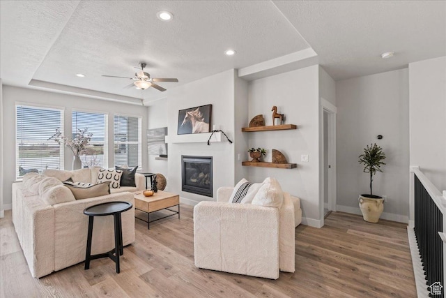 6079 W Teton Village Dr Unit 106, Herriman, UT 84096 - living room featuring a ceiling fan, a textured ceiling, a glass covered fireplace, light wood-style flooring, and baseboards