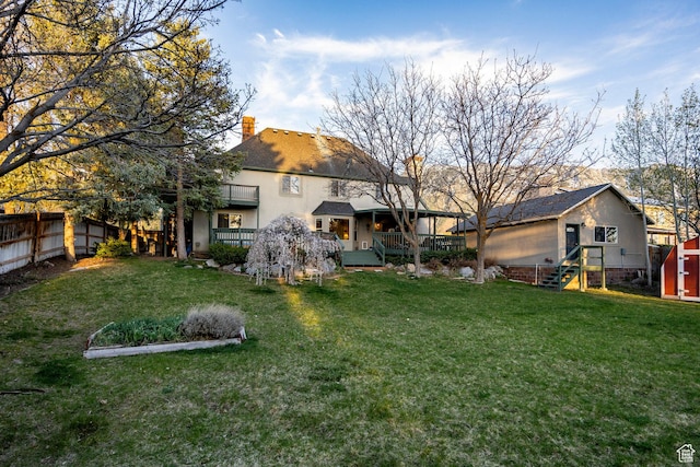 rear view of property featuring a chimney, stucco siding, fence, and a lawn